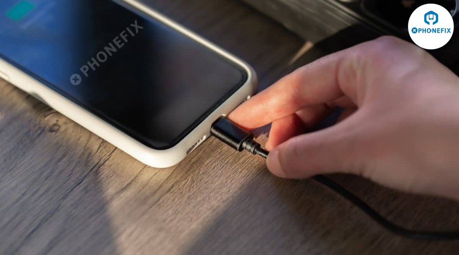 Hand connecting charging cable to smartphone on wooden desk, mobile repair concept