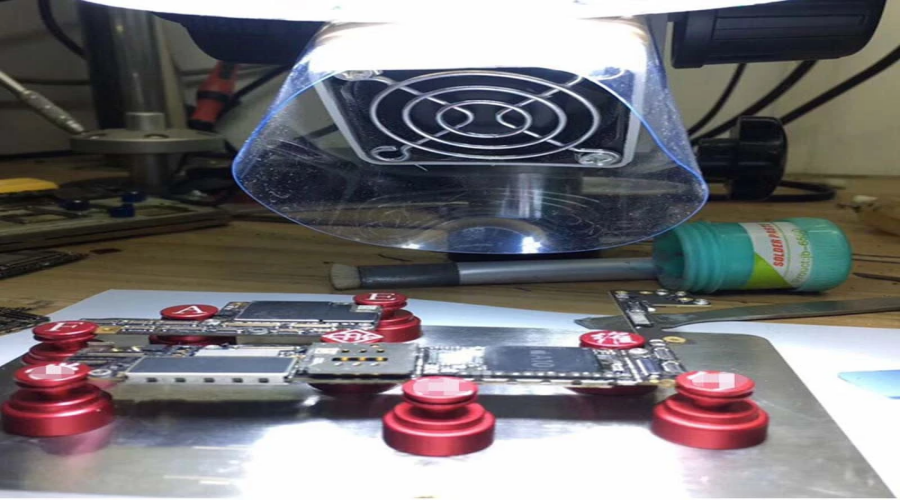 Mobile phone motherboard repair under soldering station with red clamps on workbench