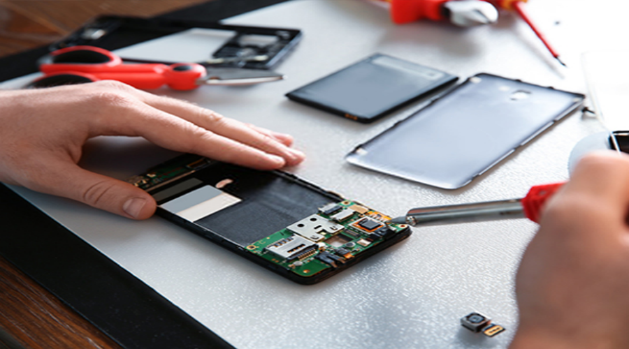 Technician repairing smartphone motherboard with soldering iron and repair tools on table