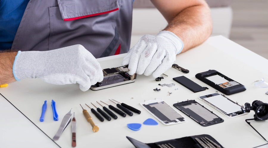 Technician repairing smartphone with precision tools and phone components on table