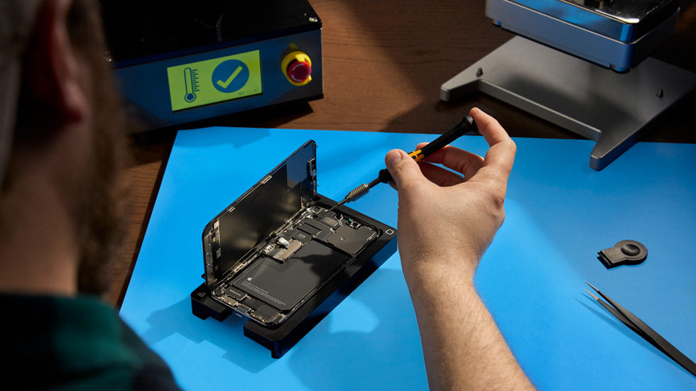 Technician using screwdriver to repair smartphone on workbench with phone repair tools.