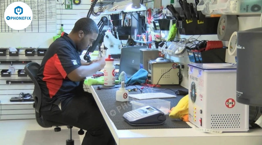 Technician repairing mobile phone at organized workbench with various phone repair tools and devices