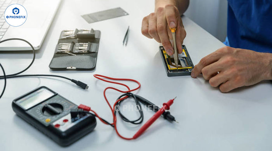 Technician repairing smartphone with screwdriver, multimeter and repair tools on table