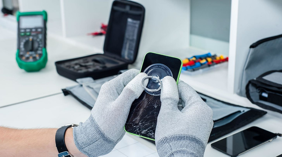 Technician wearing gloves repairing a cracked smartphone screen with repair tools on desk