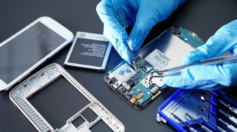 Technician in gloves repairing smartphone motherboard with tools, battery and phone parts visible