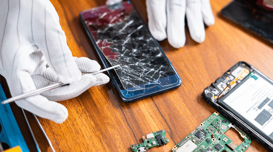 Technician in gloves repairing smartphone with cracked screen using phone repair tools on a workbench