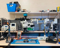 Mobile phone repair workstation with microscope, soldering tools, and testing equipment.