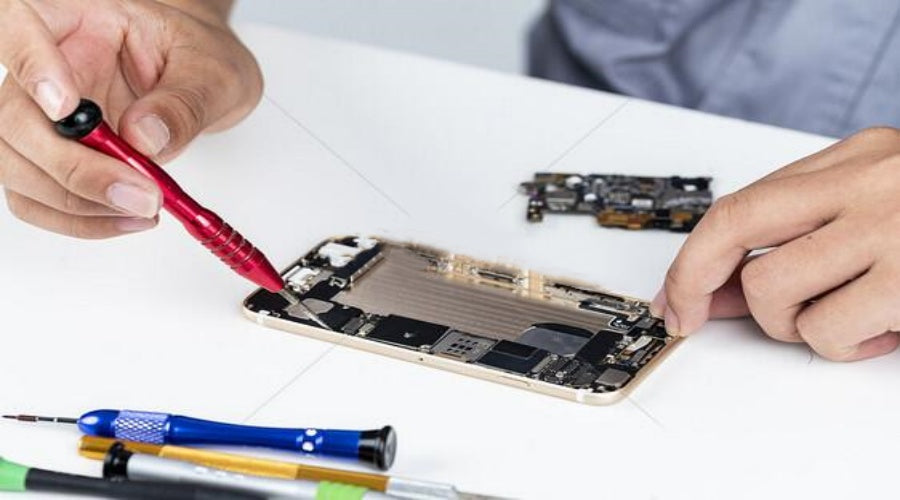 Technician using repair tools to fix a smartphone motherboard on white desk