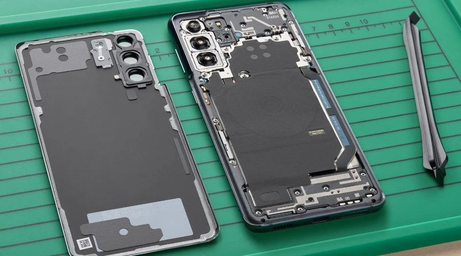 Smartphone disassembled on green repair mat with tools, showing internal components and rear cover.