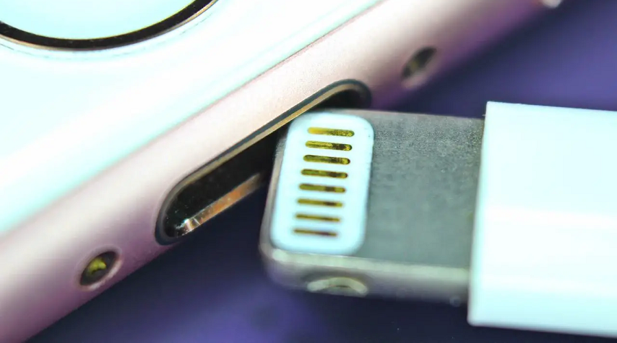 Close-up of lightning charging cable near a smartphone charging port, blue and silver tones.