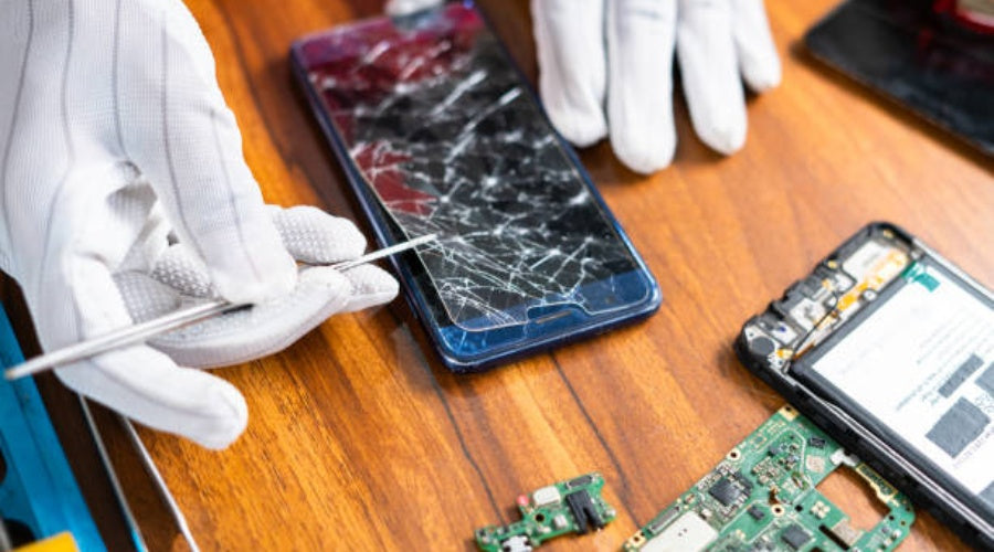 Technician repairing cracked smartphone screen with gloves and repair tools on table