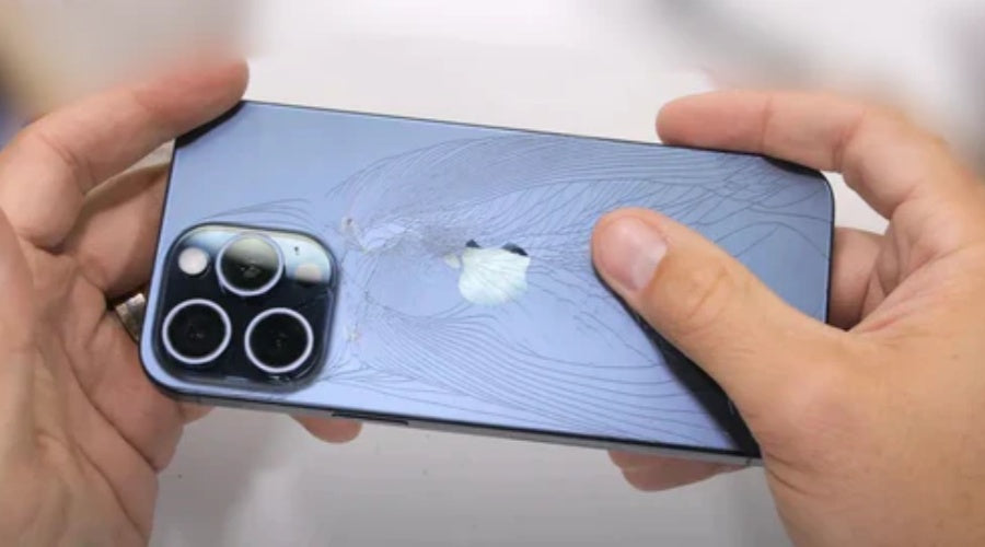 Person holding iPhone with cracked back glass near camera, mobile phone repair needed