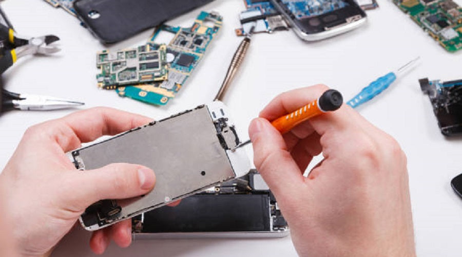 Hands using screwdriver to repair smartphone with mobile phone parts and tools on table