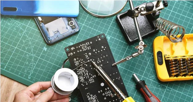 Mobile phone repair tools, circuit board, magnifying glass, screwdriver set, and soldering iron on a green work mat.